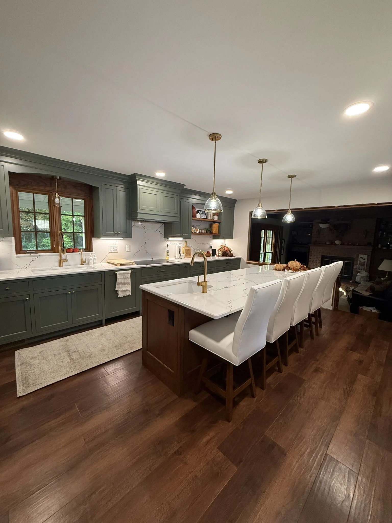 Green kitchen cabinetry around a wood island with white seating